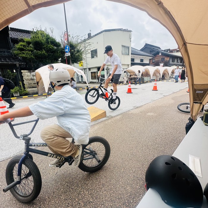 市場街の体験エリアでBMXに乗る参加者と、小さなジャンプ台を使うライダー