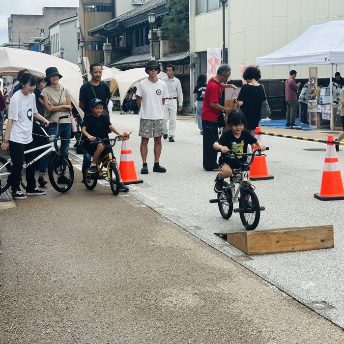 家族やライダーが見守る中、BMXで小さなジャンプ台に挑戦するキッズライダー