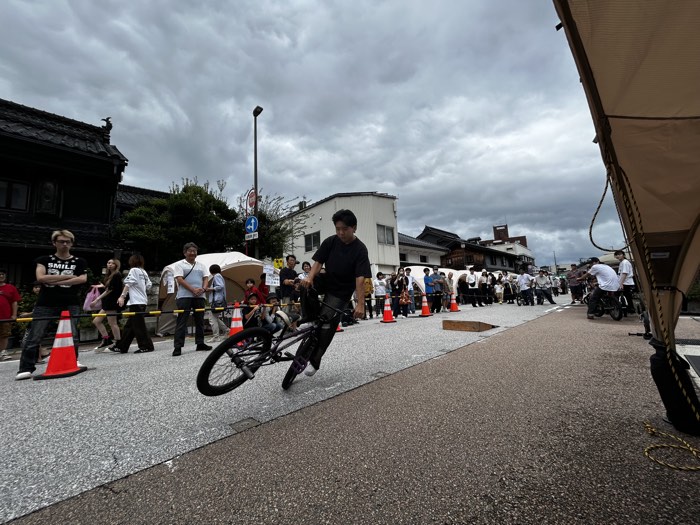 市場街の通りに集まった観客の前で、BMXのトリックを披露するライダー